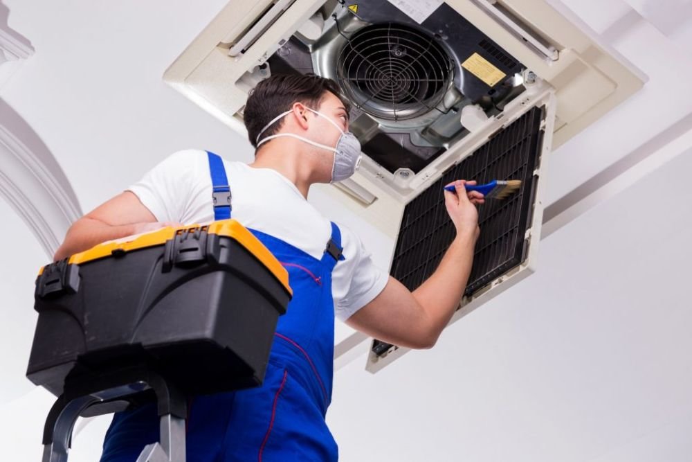 A technician in overalls and a blue work shirt fixes an air conditioner, highlighting a repair service in Long Beach, CA.